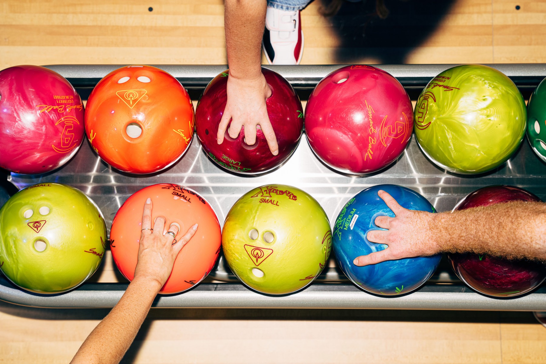Hands reaching for coloured bowling balls on the ball return at ThunderBowl