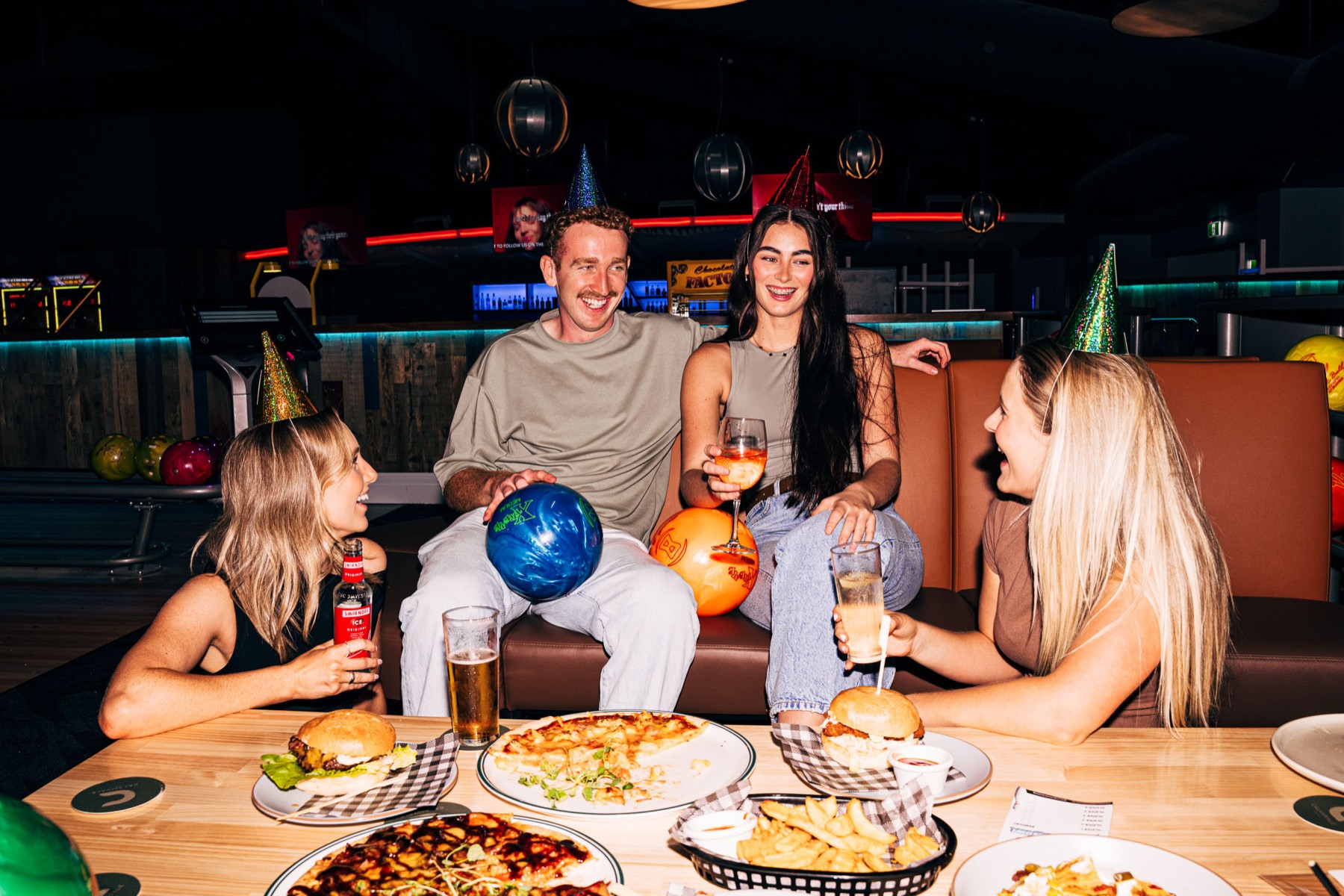 A group celebrating with party hats, food and bowling balls in the booth seating at ThunderBowl Calamvale