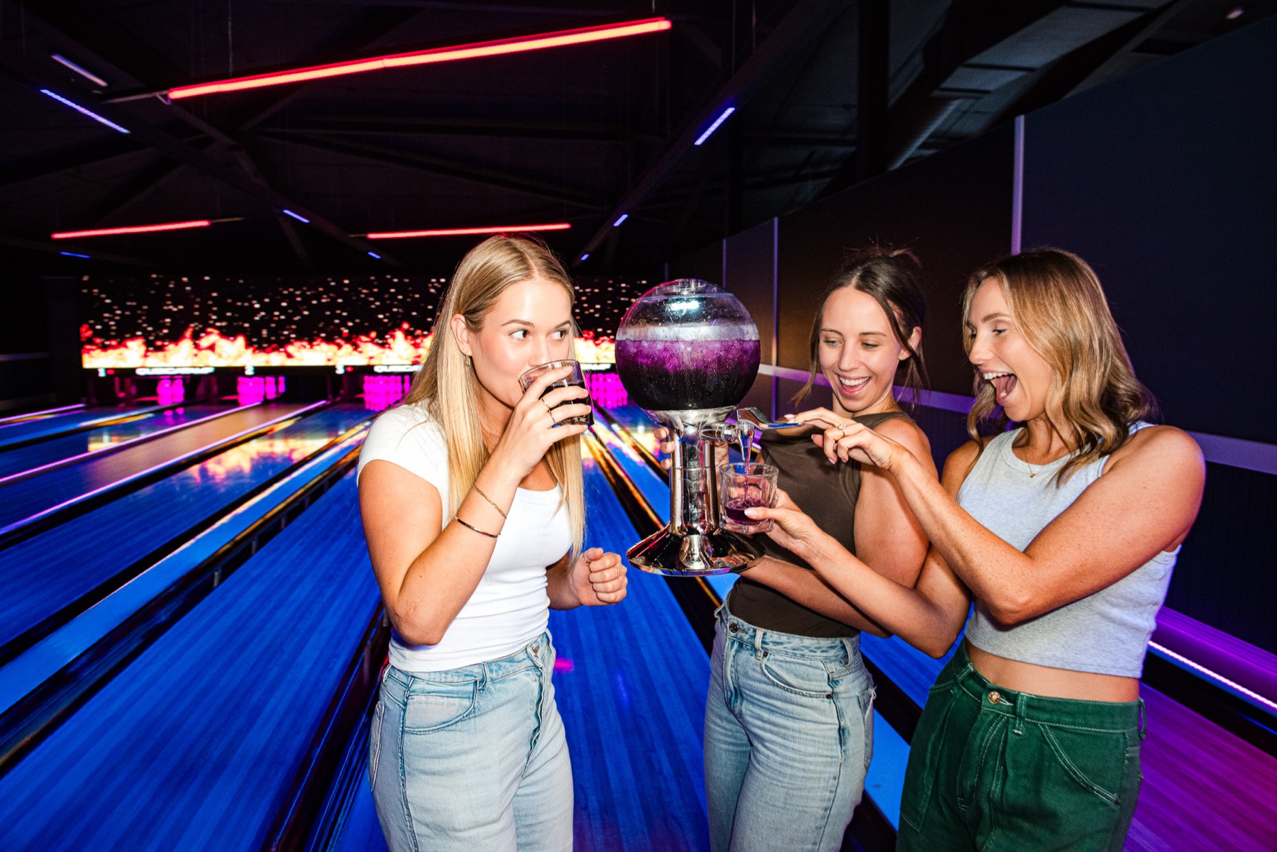 A group of friends pouring drinks from a share tower beside the lanes at ThunderBowl Calamvale